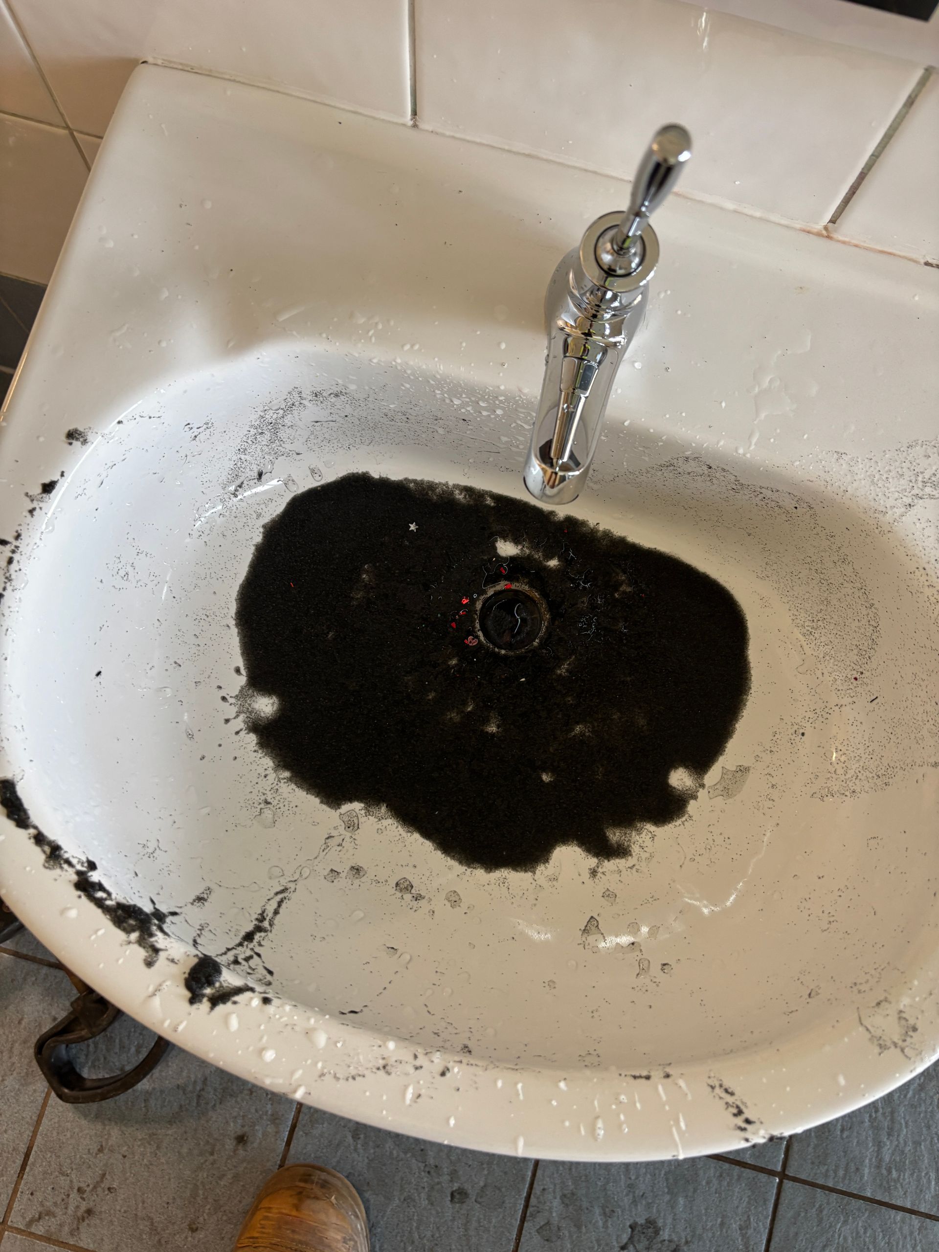 Under-sink view: black garbage disposal, white pipes, plumbing, electrical outlet, inside a white cabinet.