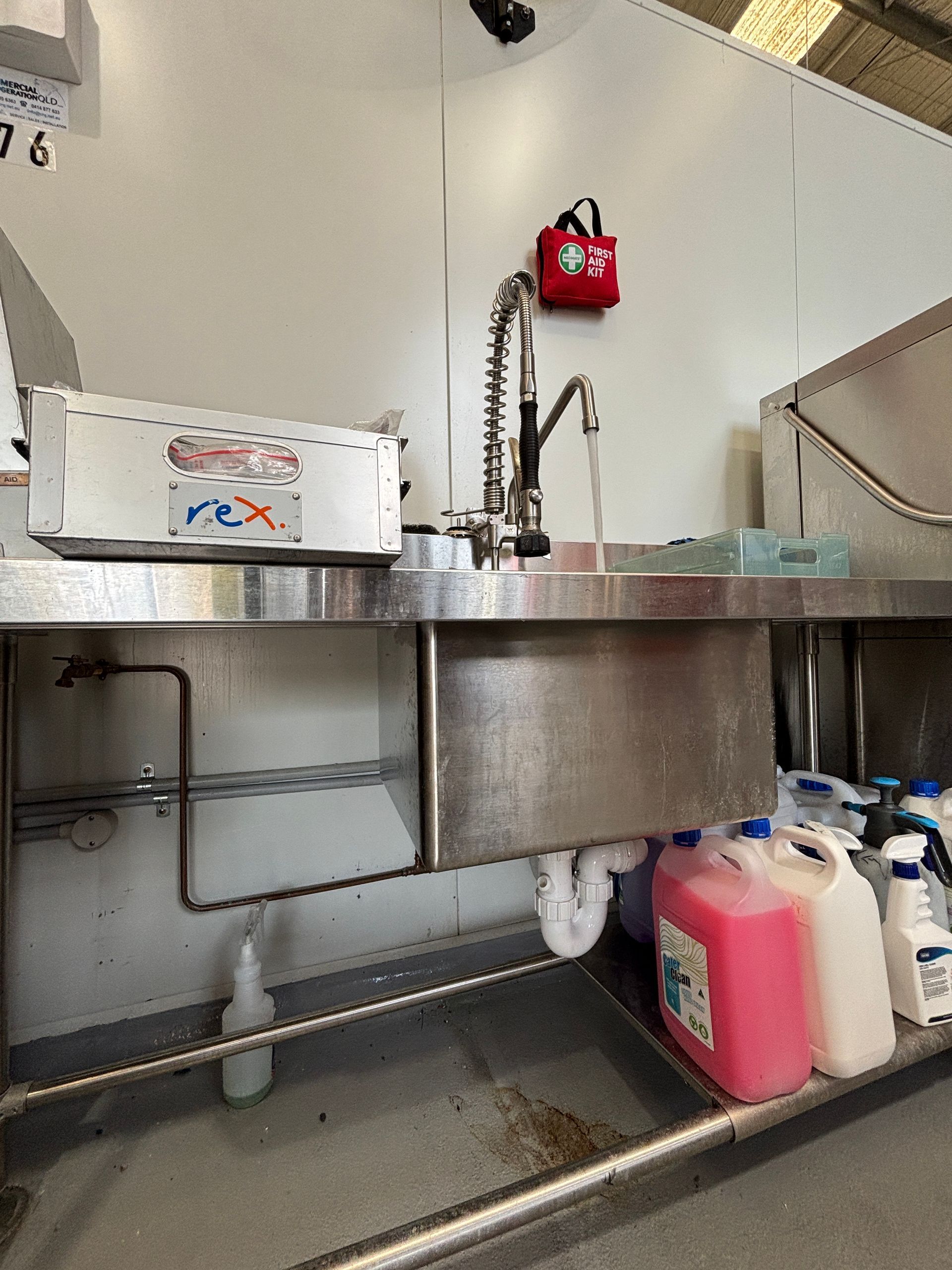 Stainless steel sink with faucet, cleaning supplies, and mounted fire extinguisher in a commercial setting.
