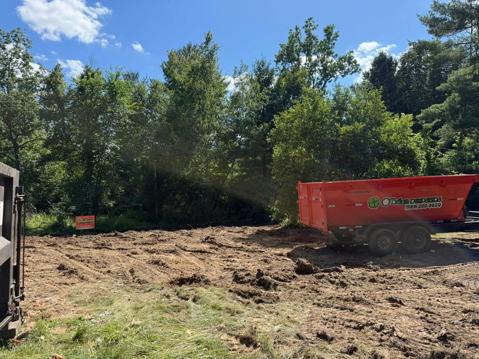 Cleared land with an orange trailer, trees in the background, blue sky.