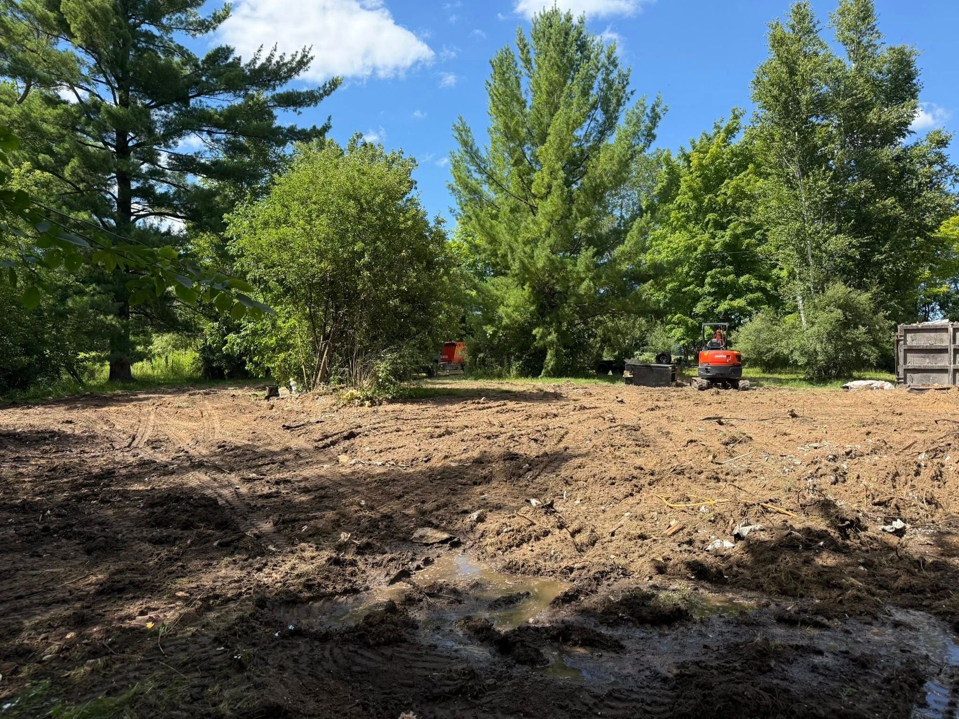 Brown dirt field cleared for construction; trees in background; two small excavators present.