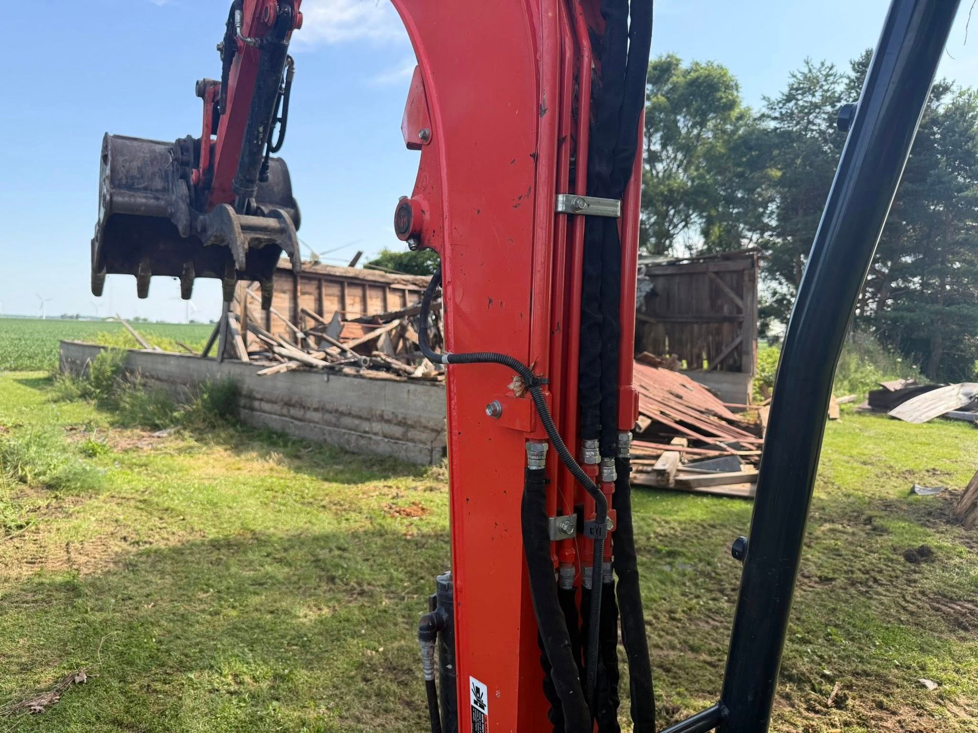Red excavator demolishing a wooden structure in a grassy field.