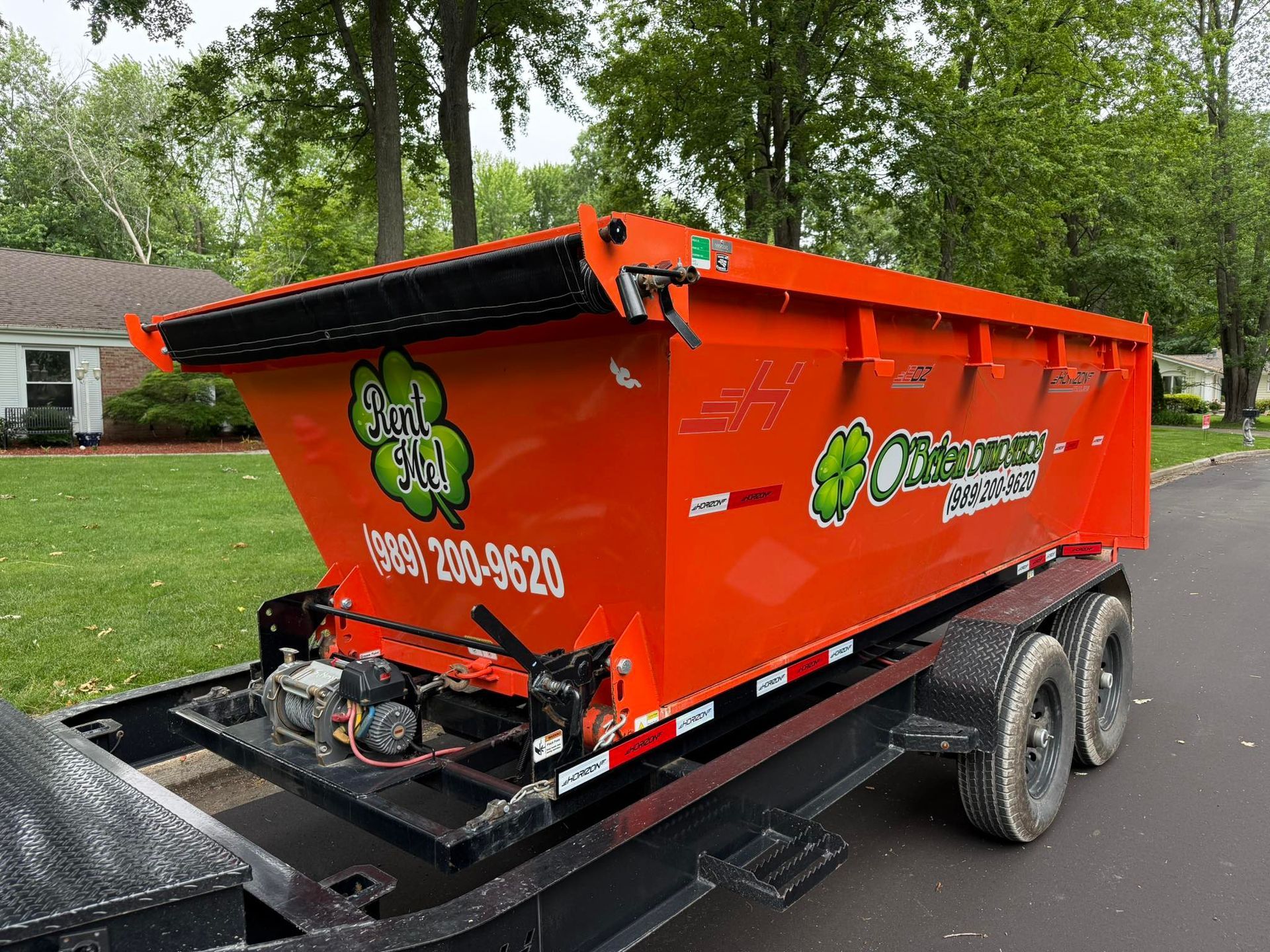 Orange dumpster trailer with business logo parked on a street.