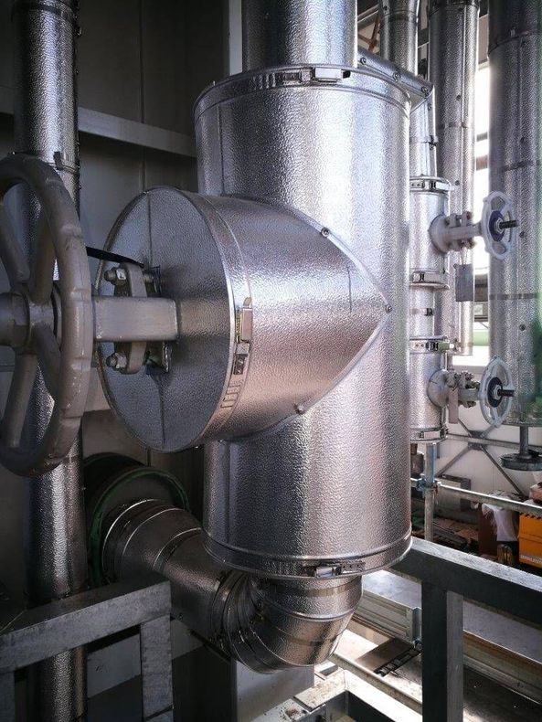 Condotti e tubazioni industriali in metallo in un ambiente di fabbrica, con un'ampia camera cilindrica lucida.