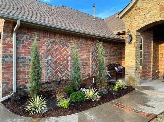 A red brick house exterior featuring two recessed herringbone brick panels and a manicured garden bed with small trees.