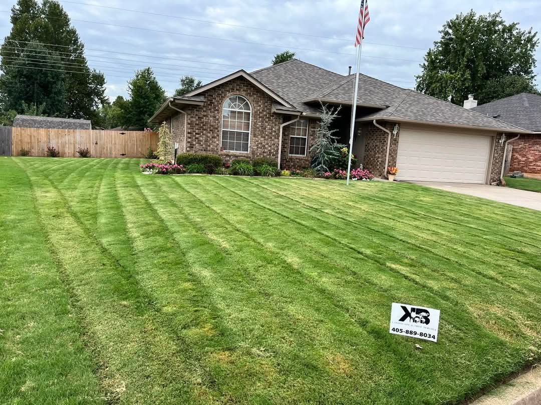 A brick residential house with a neatly mowed lawn and an American flag on a flagpole in the front yard.