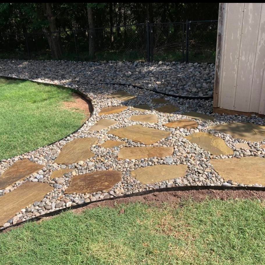 A stone stepping stone path set in gravel, bordered by manicured green grass and a garden shed.