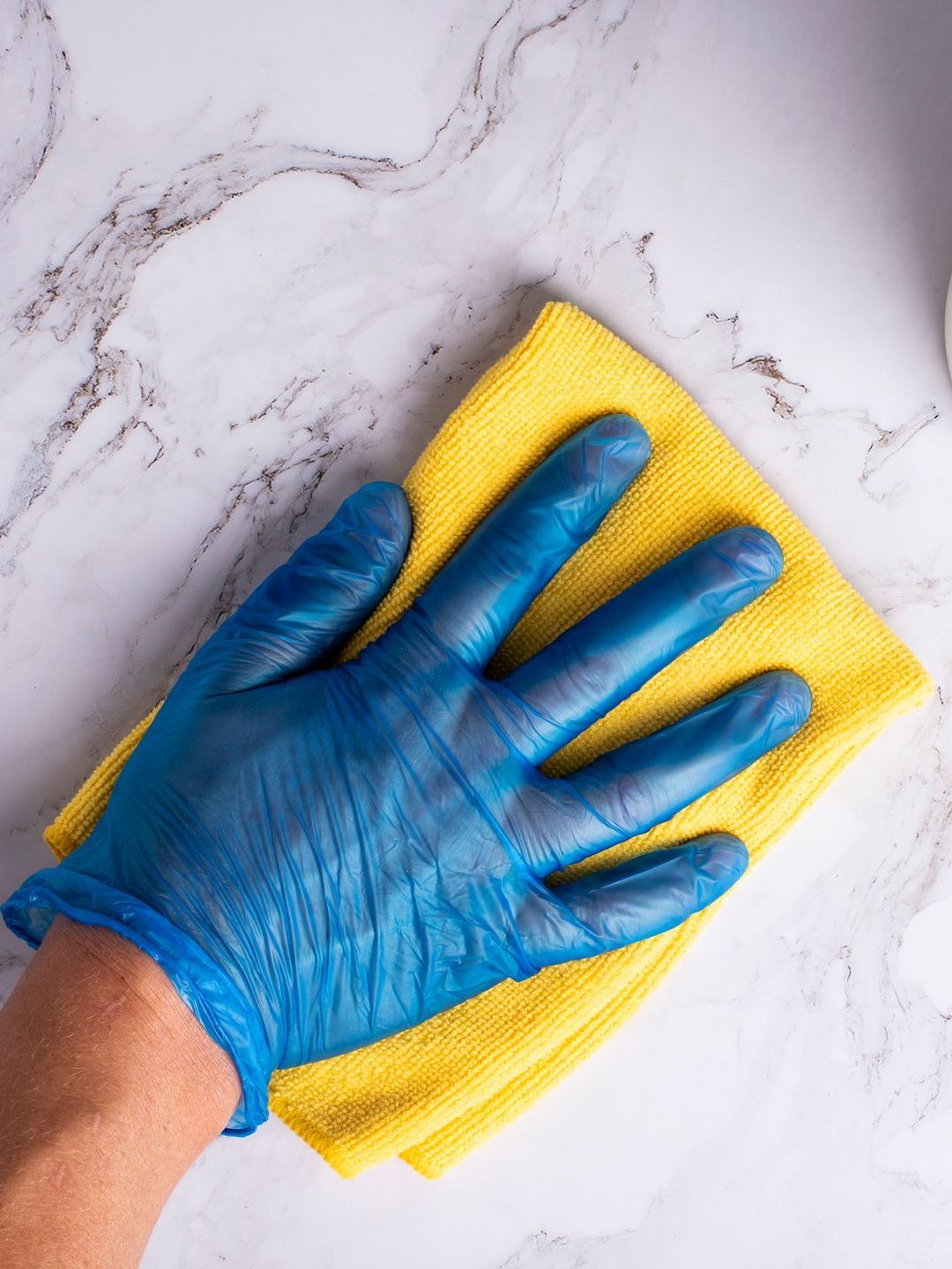 A person wearing blue gloves is cleaning a counter with a yellow cloth.