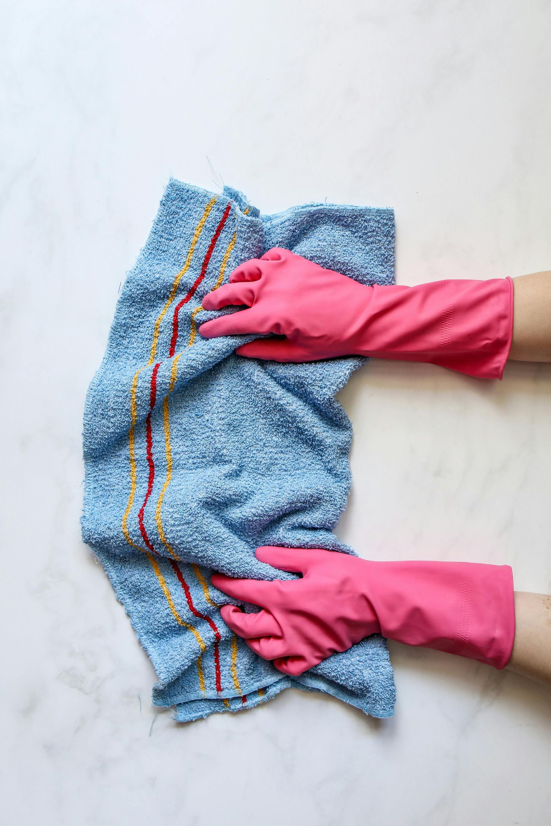A person wearing pink rubber gloves is cleaning a blue towel.