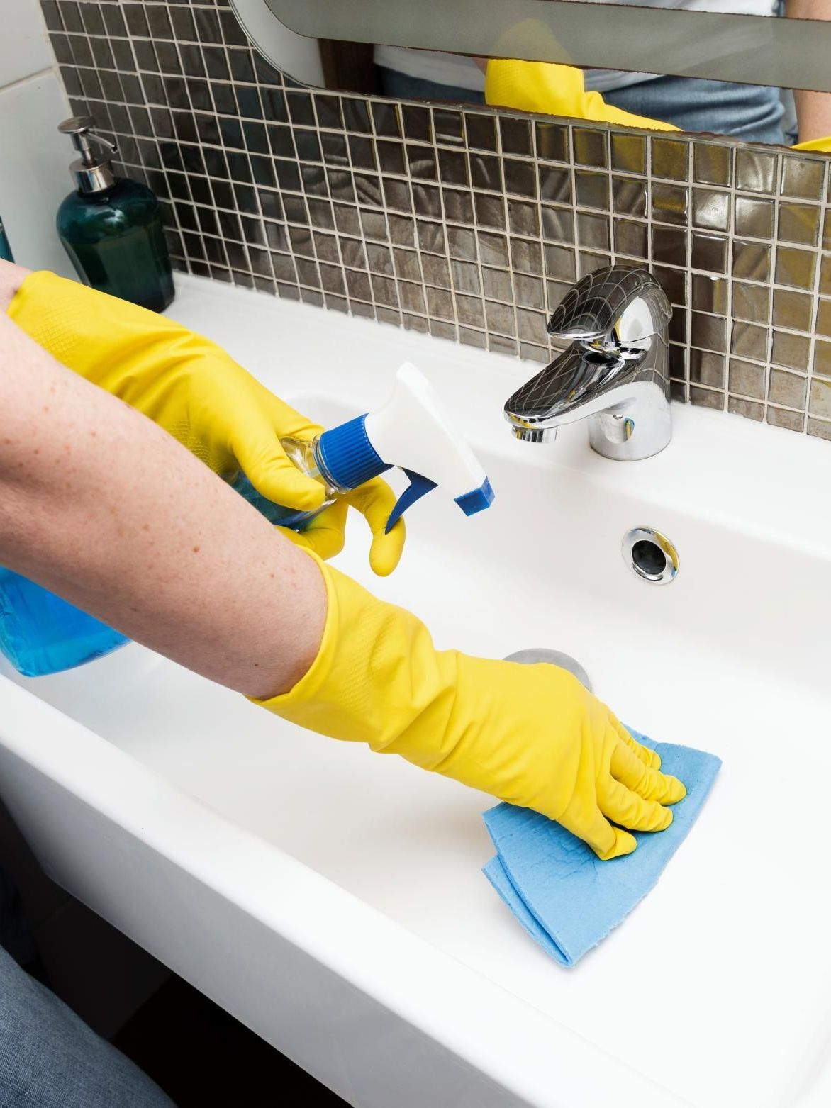 A person wearing yellow gloves is cleaning a bathroom sink.