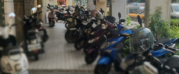 Motorcycles parked in a row on a sidewalk; various colors including red, blue, and black.