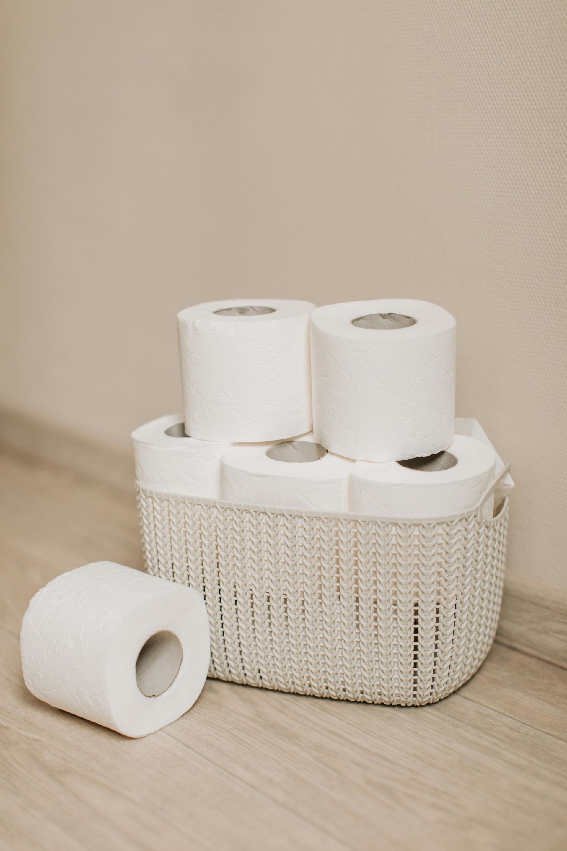 White toilet paper rolls in a basket on a light-colored wooden floor, near a beige wall.