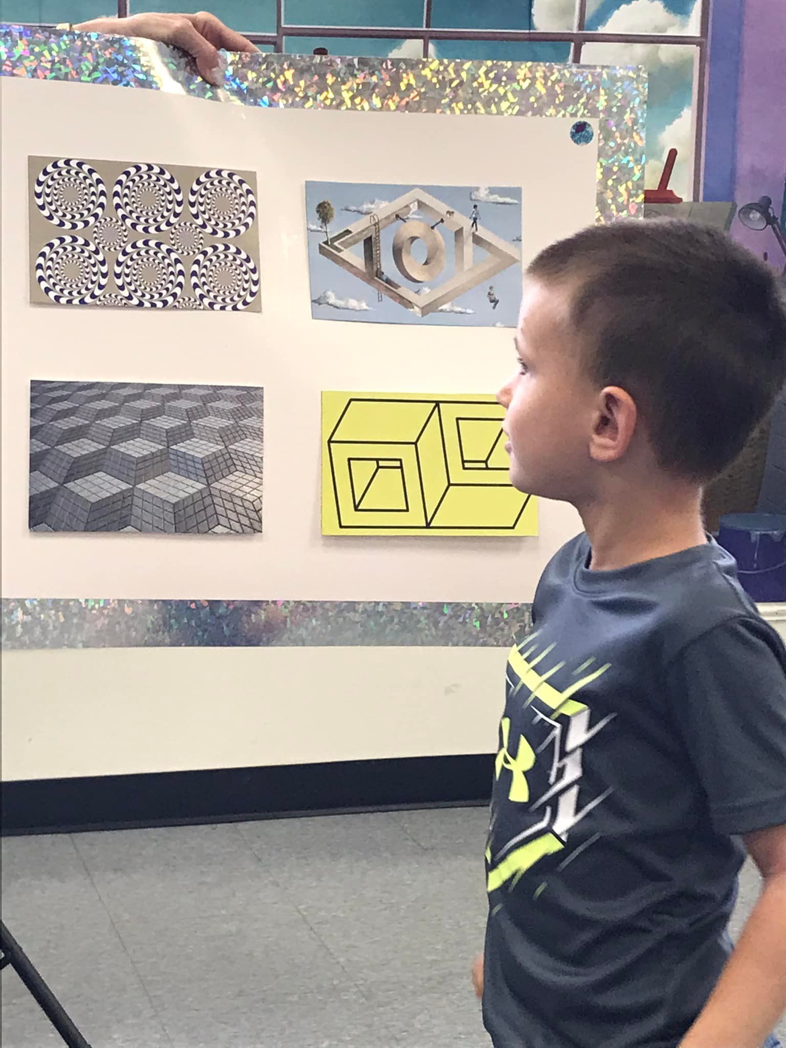 A young boy looking at optical illusions on a display board; room setting.