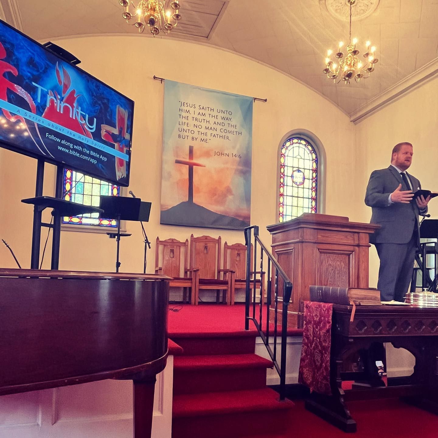 Man preaching at Trinity Church with a banner, cross, and screen displaying