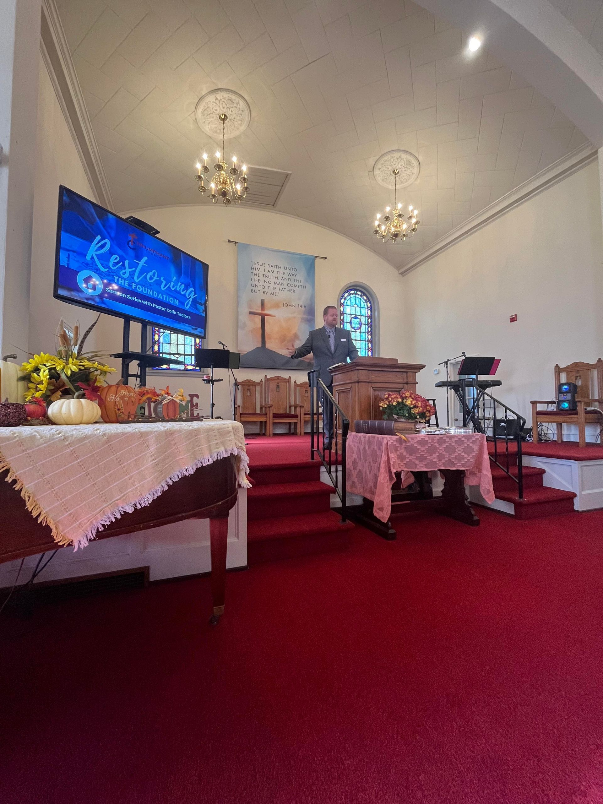 A man stands at a wooden podium inside a church. A large screen displays