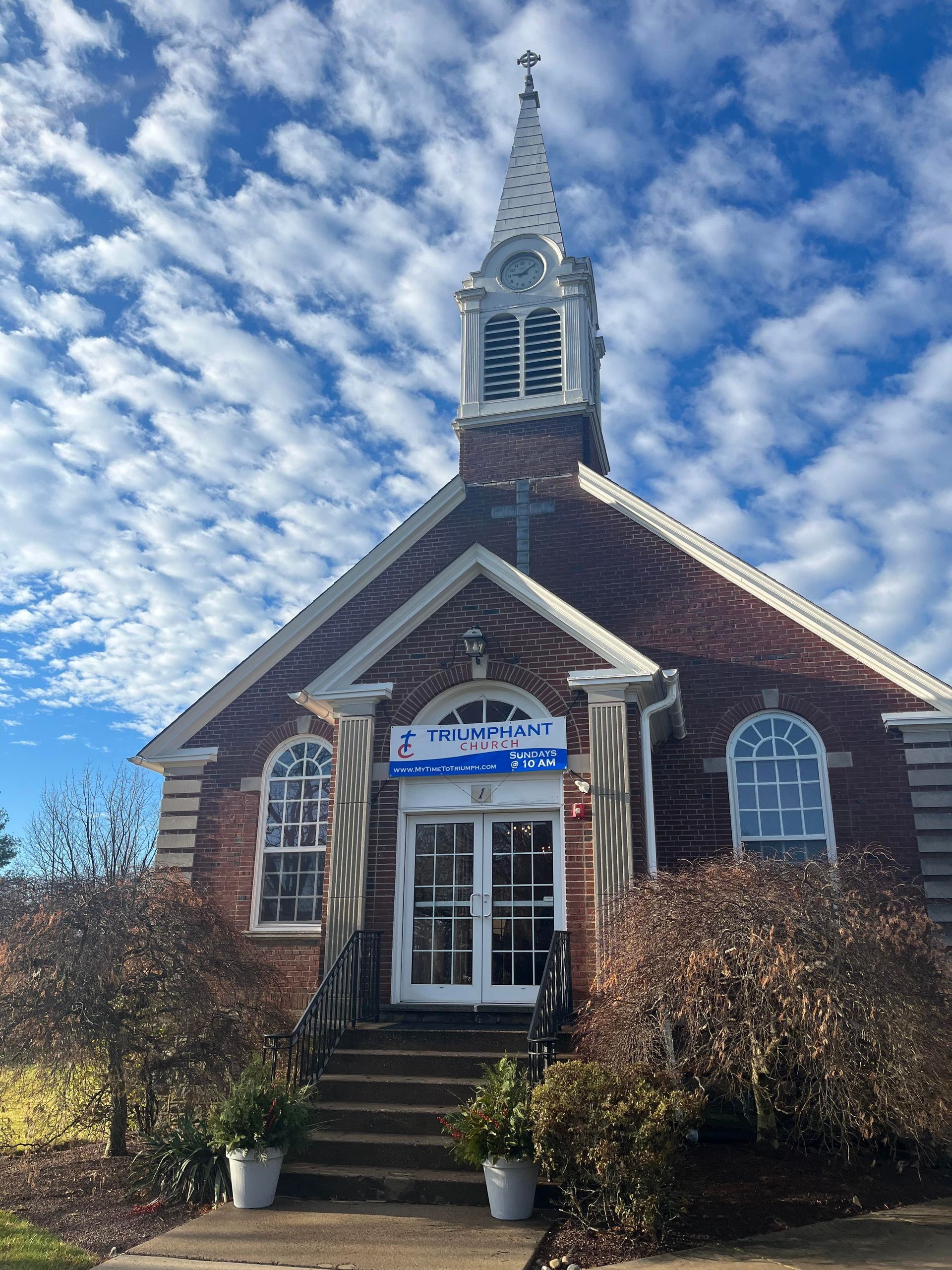 Brick church with steeple and steps leading to the door under a blue sky.