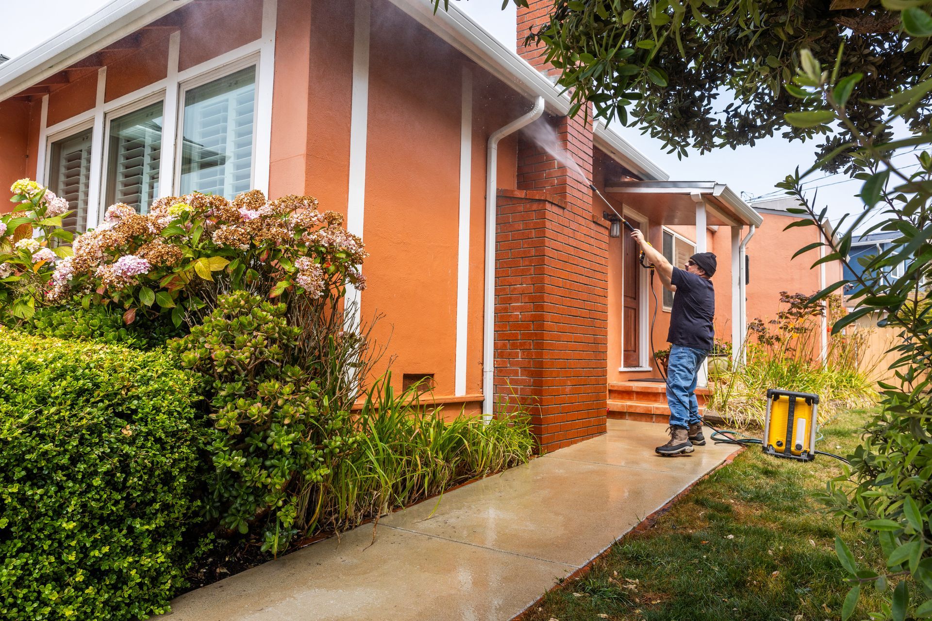 A man is cleaning a brick house with a pressure washer.