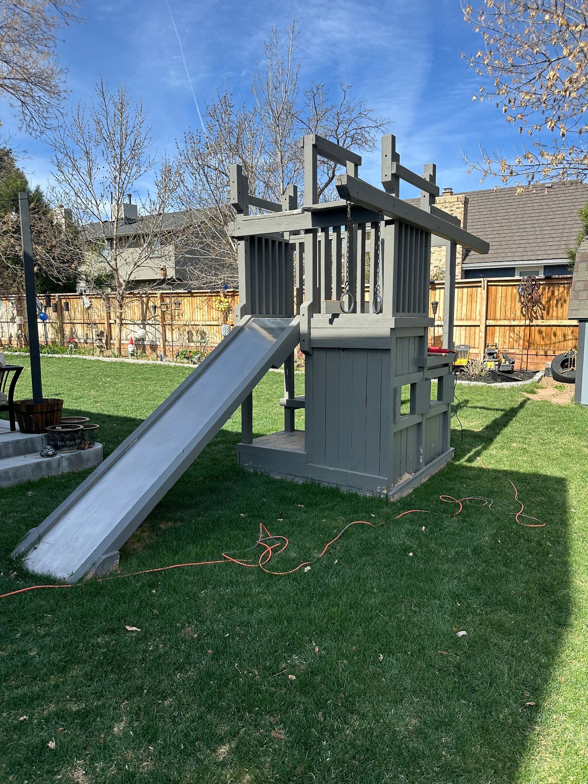 Gray wooden playset with a slide in a grassy backyard. A before picture taken in Louisville, CO