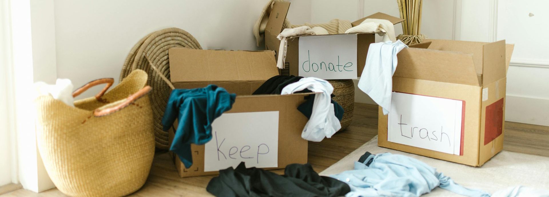 A room filled with cardboard boxes filled with clothes and a basket.