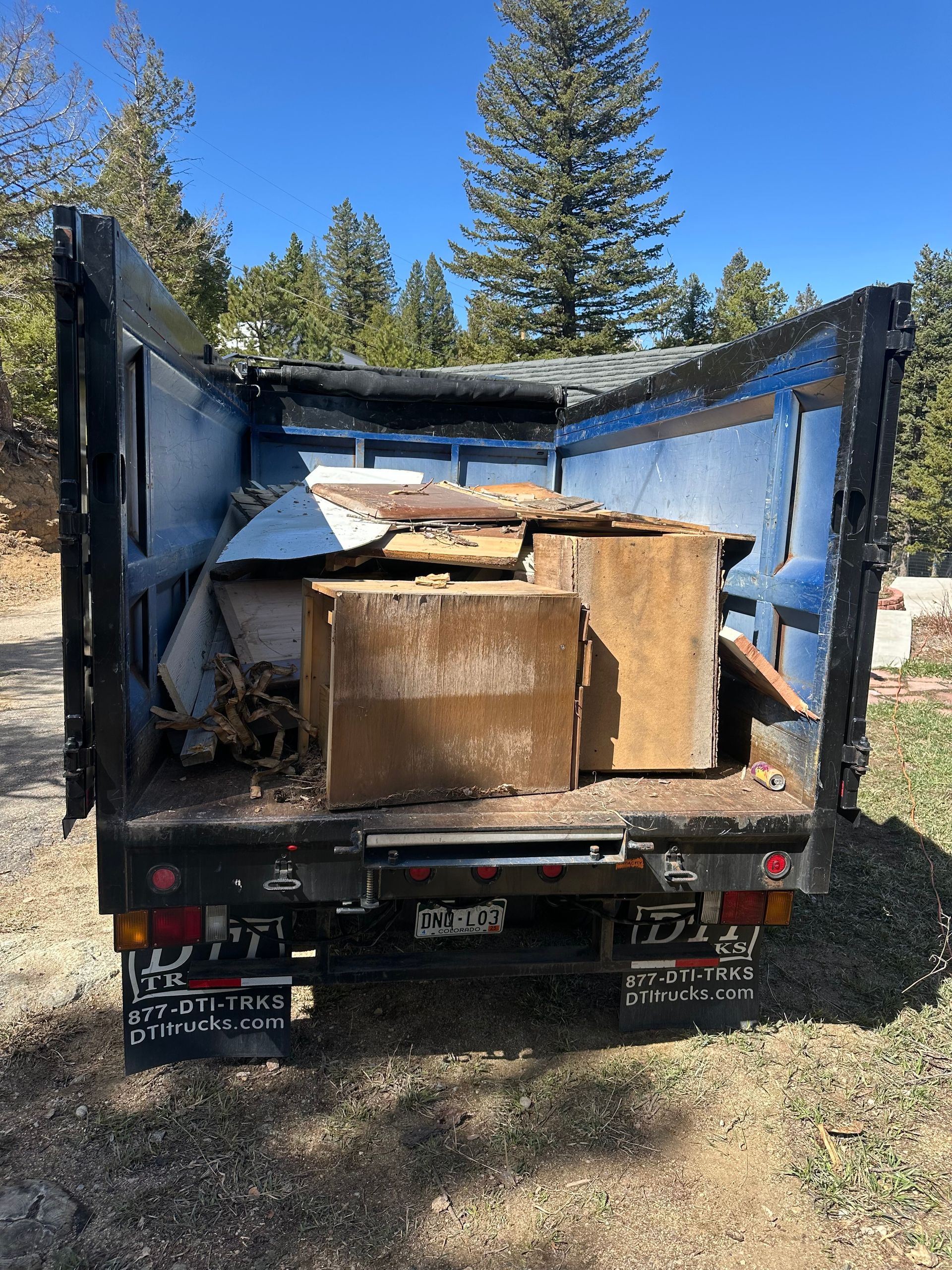 A Junk Runners truck bed filled with wooden debris, likely construction waste, outdoors on a sunny day in Louisville, CO.