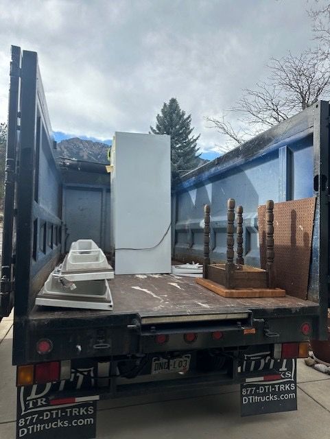 A truck bed loaded with a refrigerator, furniture, and other items, likely for disposal. Photo taken in Boulder, CO.