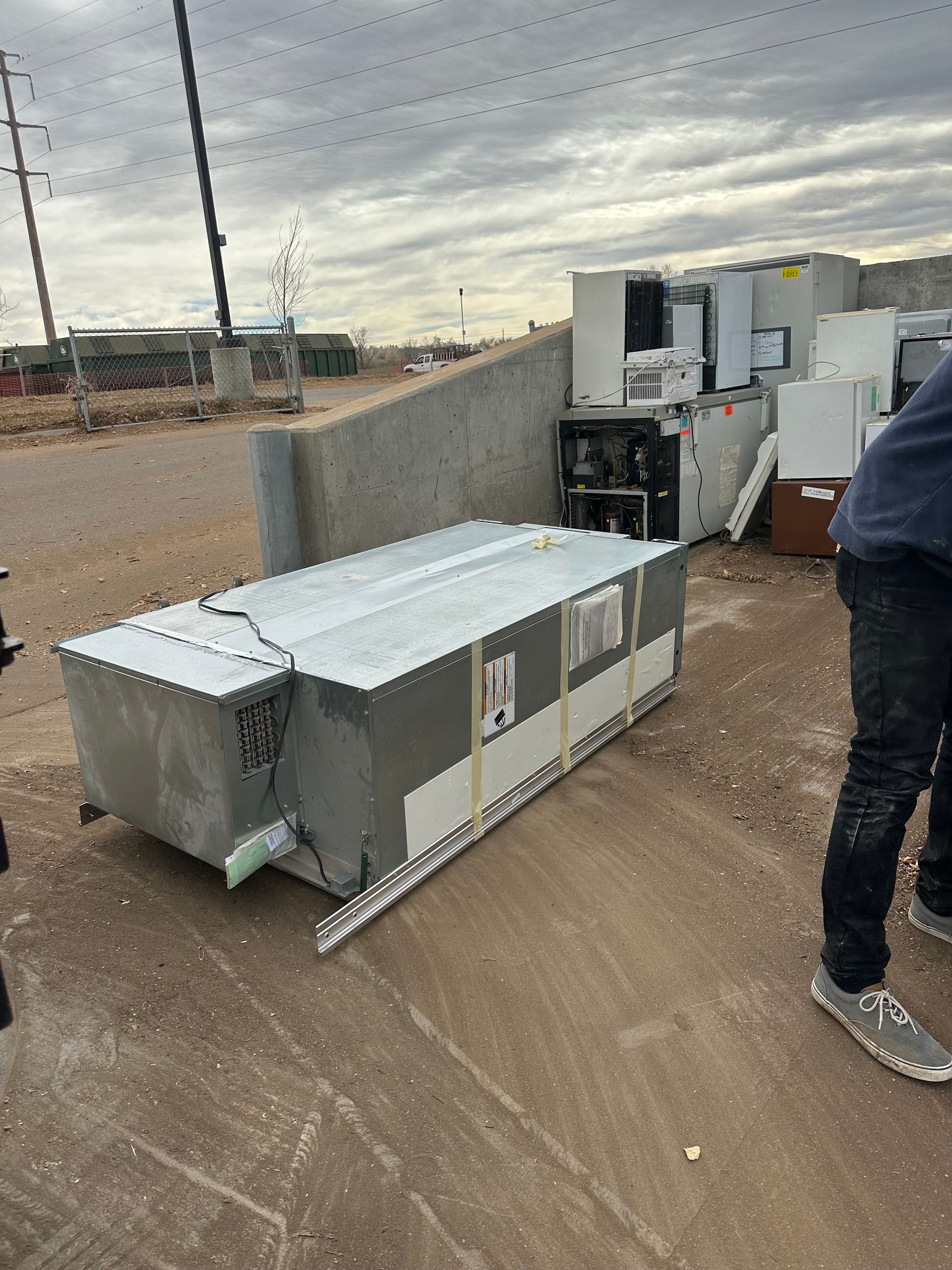 Large, rectangular industrial unit on ground outdoors. Person in frame. Other units and gray sky visible.