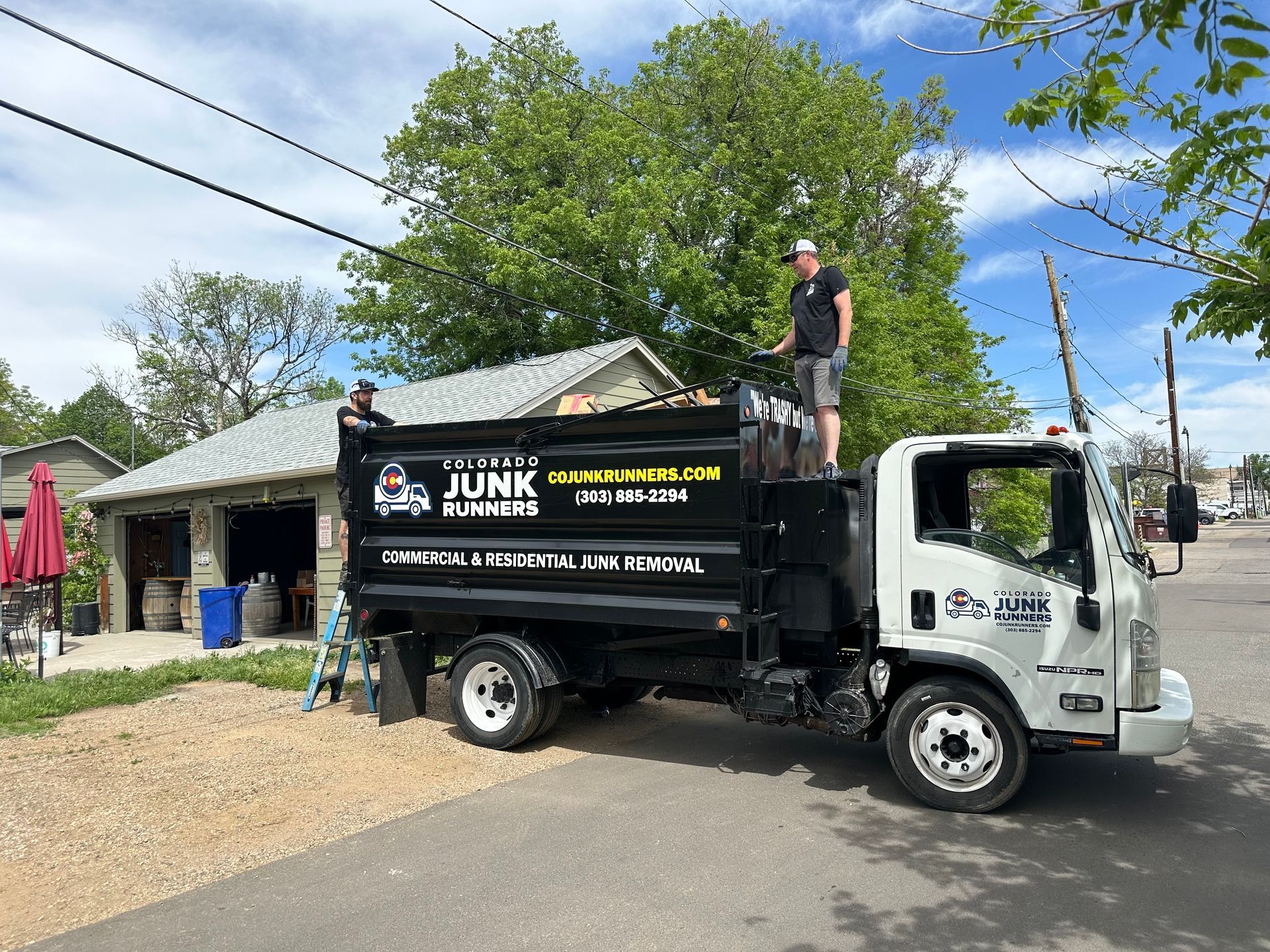 Two men loading debris into a black and white Colorado Junk Runners truck on a street at a brewery in Louisville, CO.
