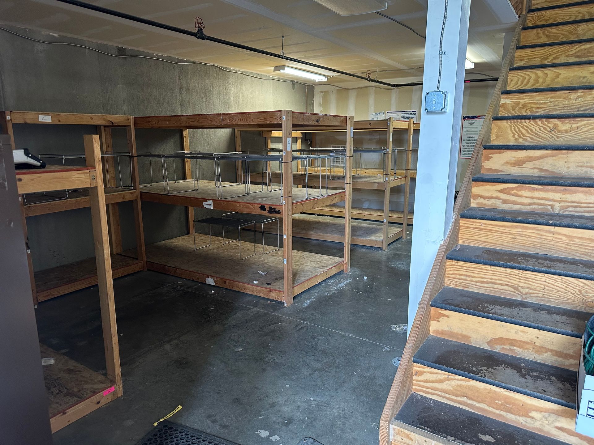 Storage room with wooden shelves and stairs. Concrete floor, neutral color palette.