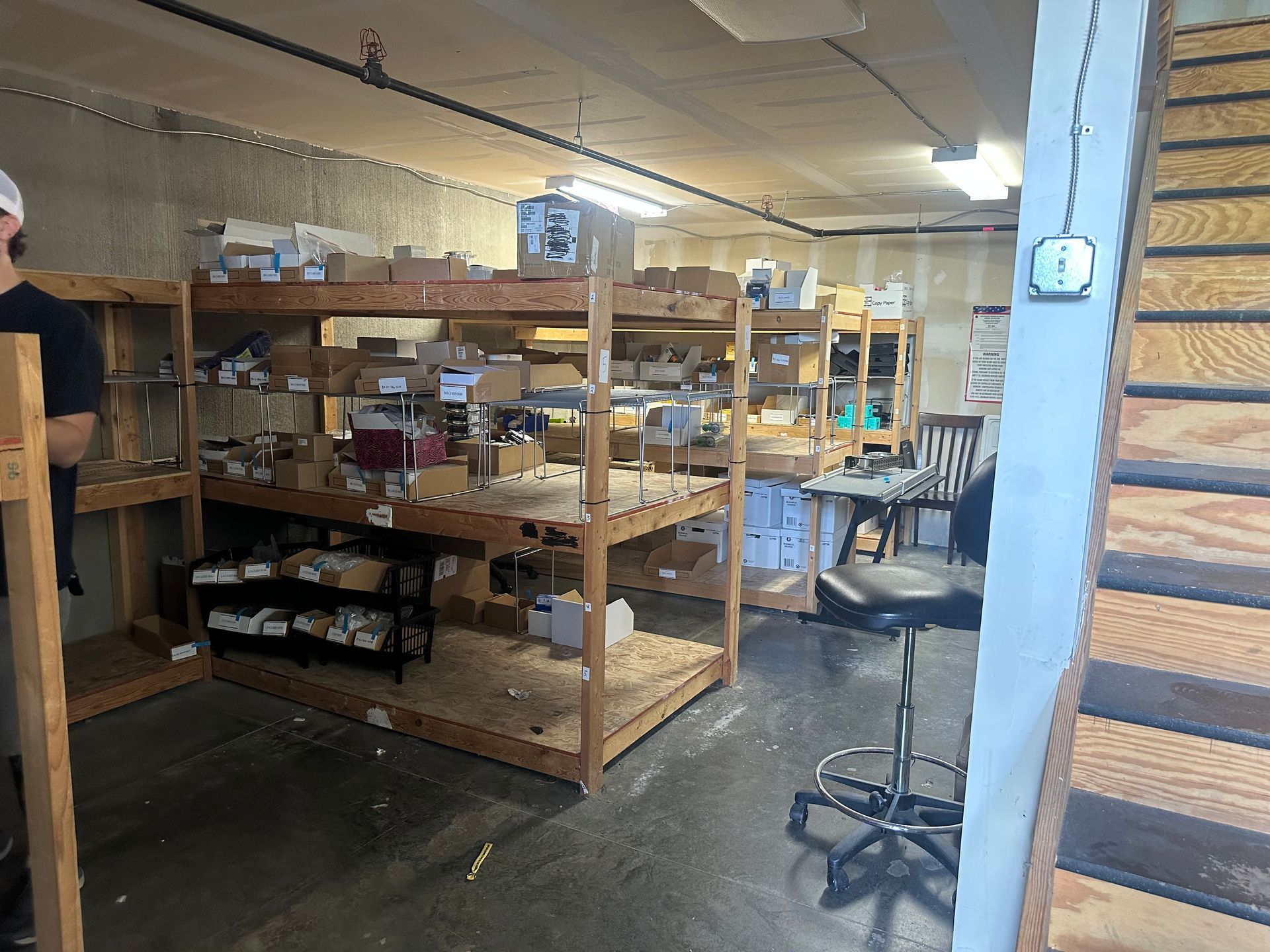 Workshop interior with wooden shelves stocked with boxes and supplies. A staircase is on the right.