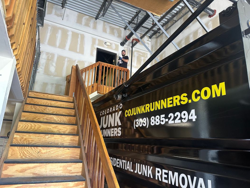 A Colorado Junk Runners truck parked next to interior wooden stairs; a person stands on a landing.