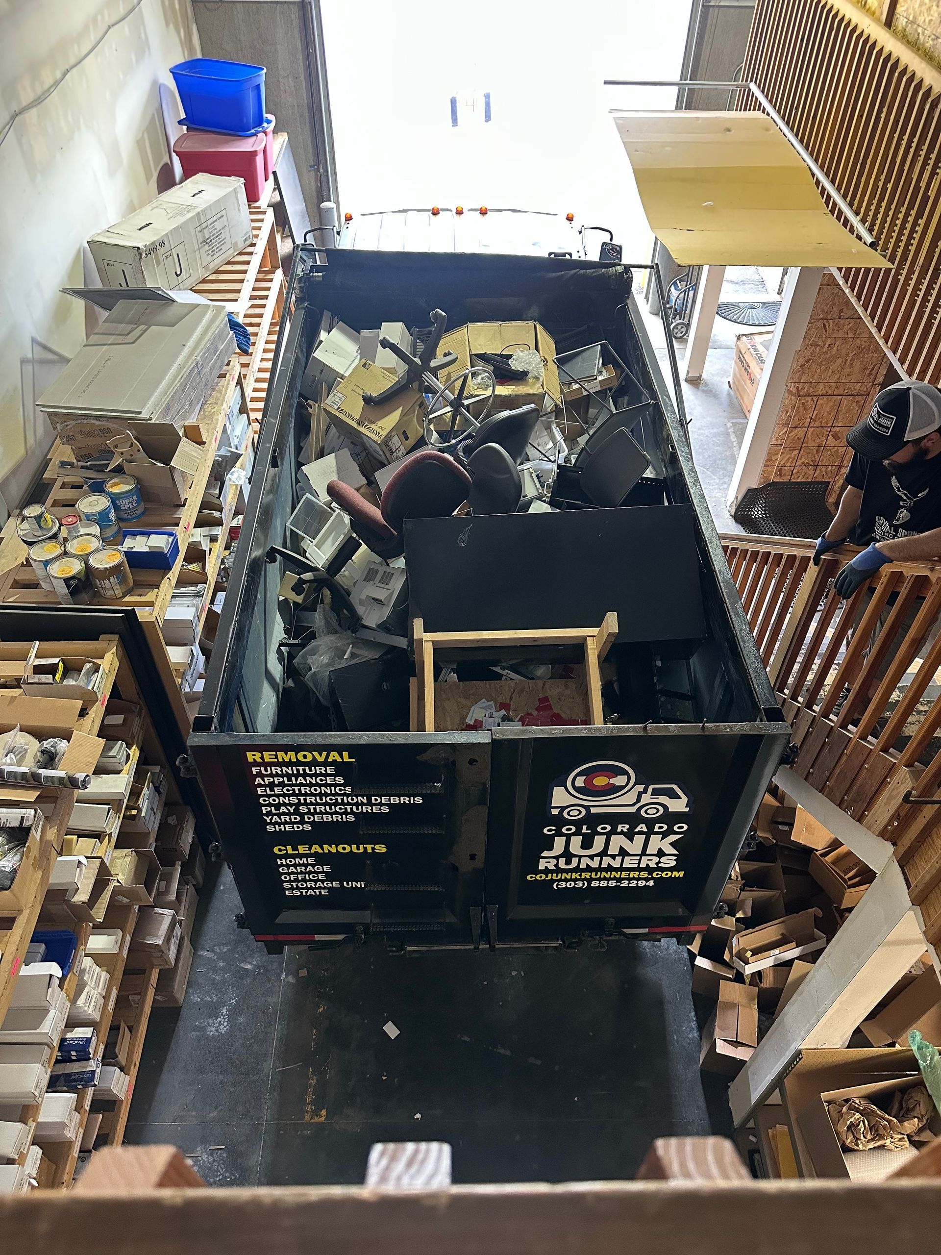 Colorado Junk Runners truck filled with debris in narrow space. Brick walls and stairs visible, possibly interior.