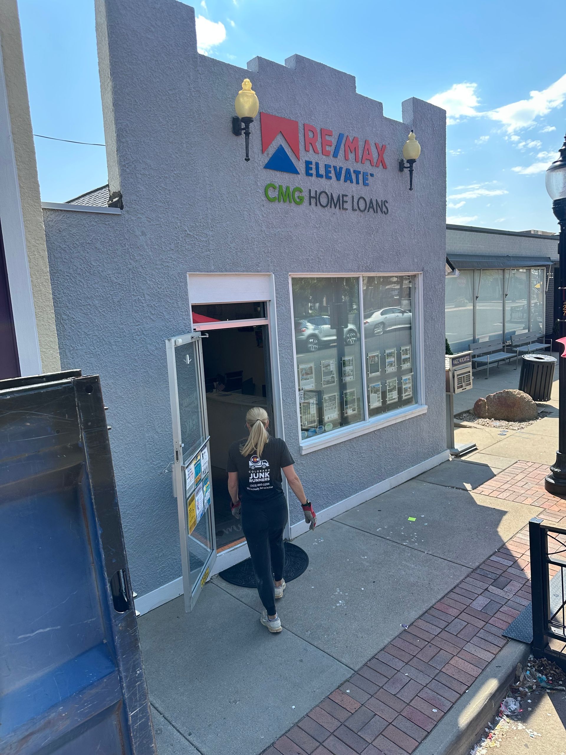 Junk Runner exits the RE/MAX Elevate and CNG Homeloans storefront, a small building on a sidewalk.