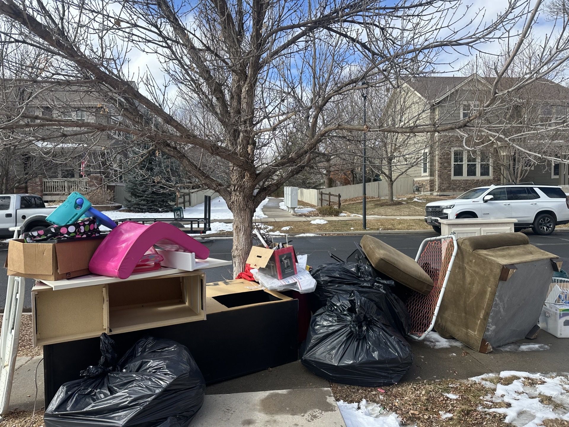 Pile of discarded furniture and trash on a sidewalk, including black bags, boxes, and a mattress in Broomfield, CO.