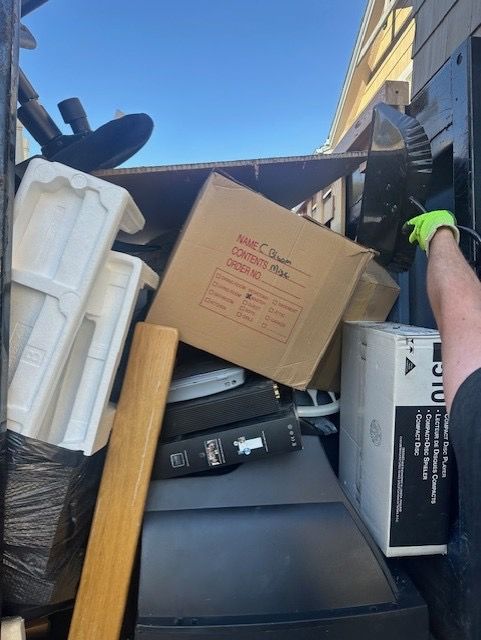 A truck bed filled with assorted items: boxes, electronics, and packing materials, with a gloved hand reaching in.