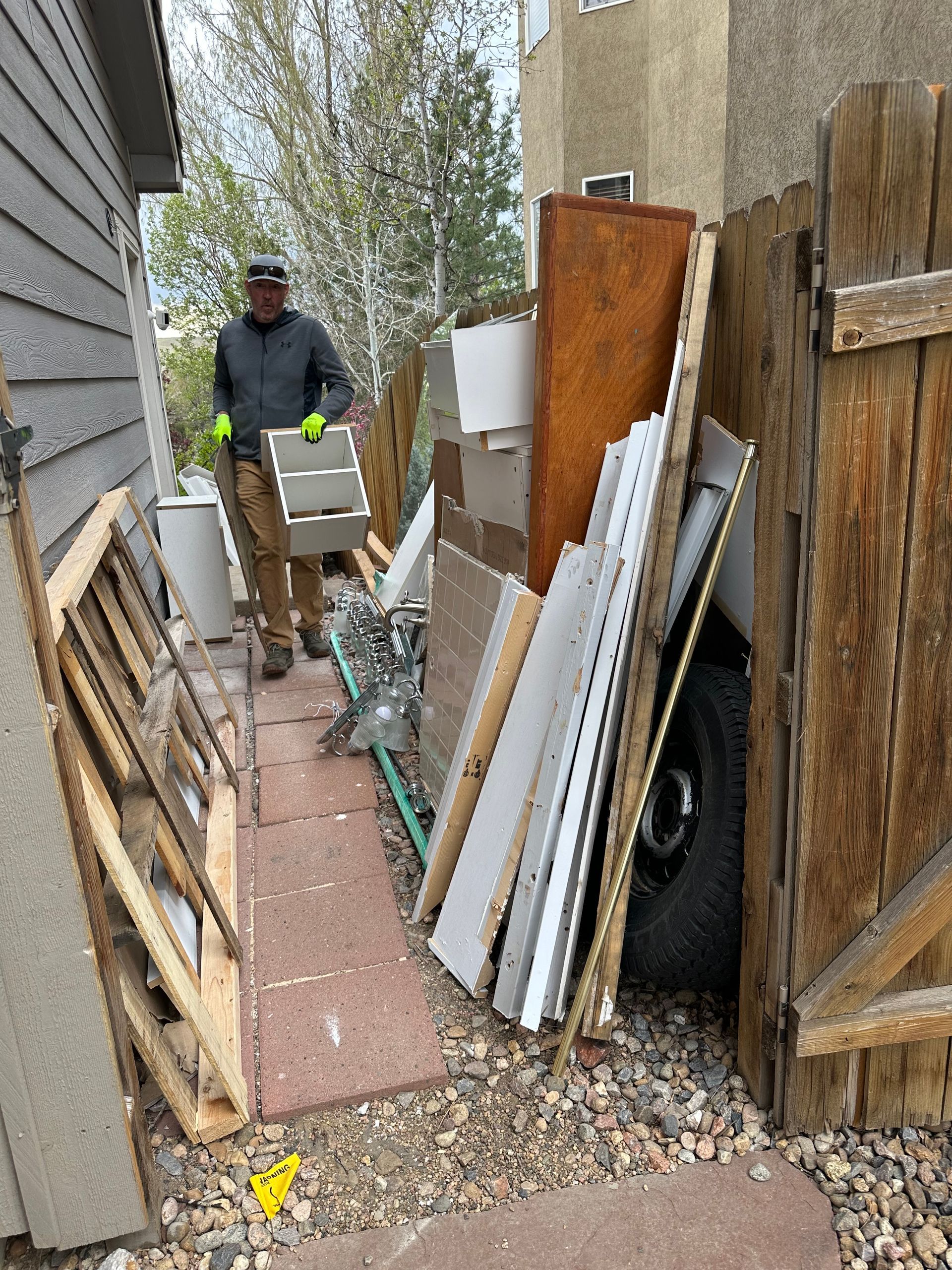 Man carrying debris, standing near a pile of trash next to a wooden fence and building in Erie, CO.