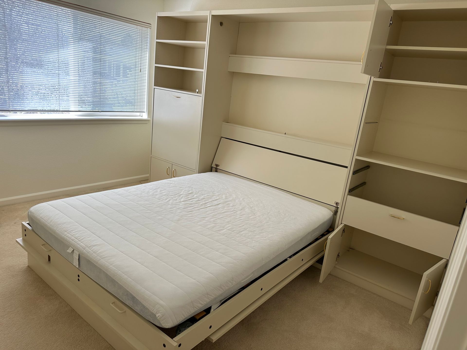 Cream-colored wall bed with open mattress. Shelves and storage on either side, near a window.