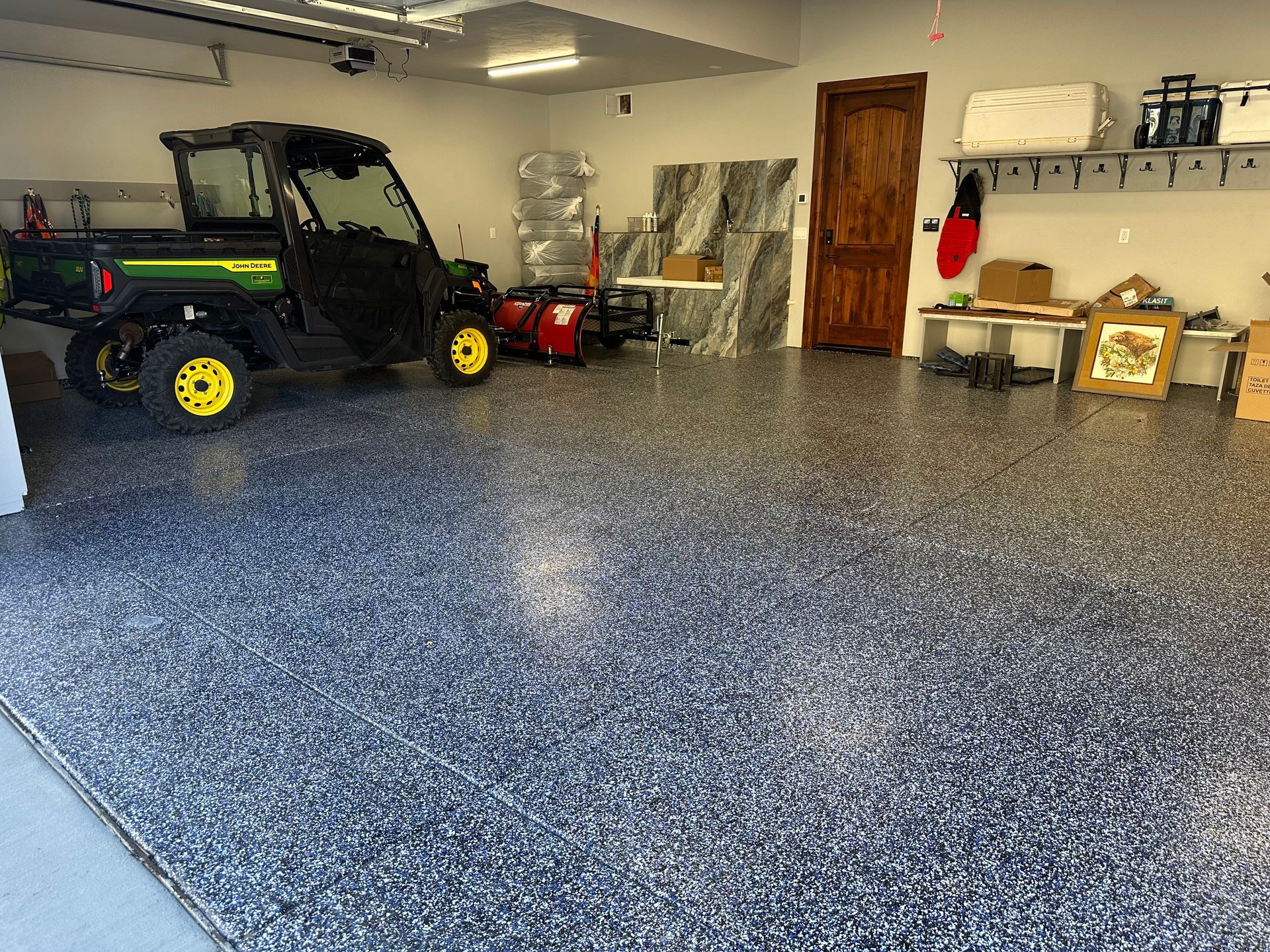 Garage with a dark epoxy floor, John Deere utility vehicle, snowblower, and storage shelves.