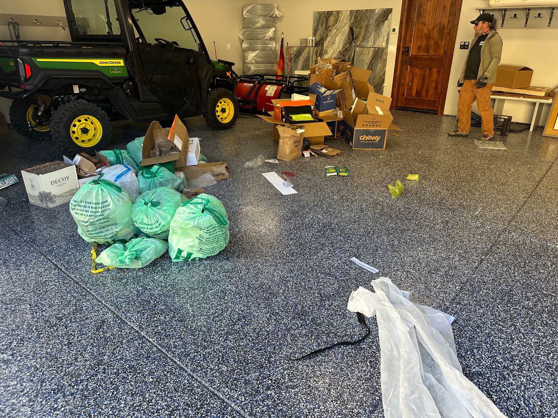 Garage with a John Deere utility vehicle, trash bags, cardboard boxes, and a person.