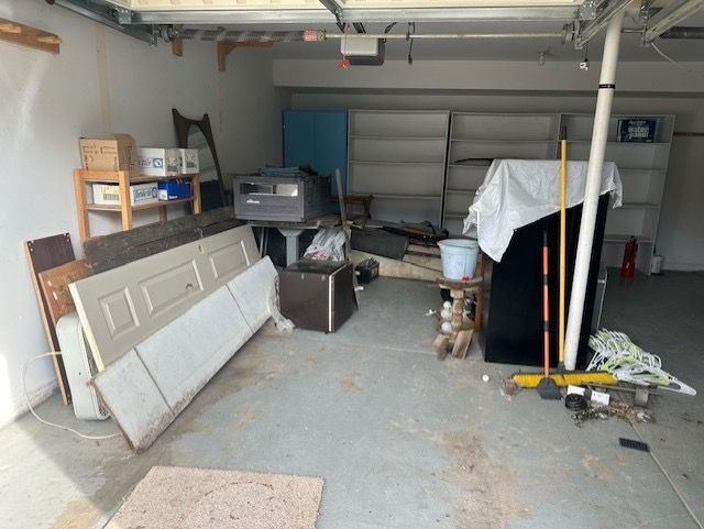 Cluttered garage with junk, shelves, and a closed garage door.
