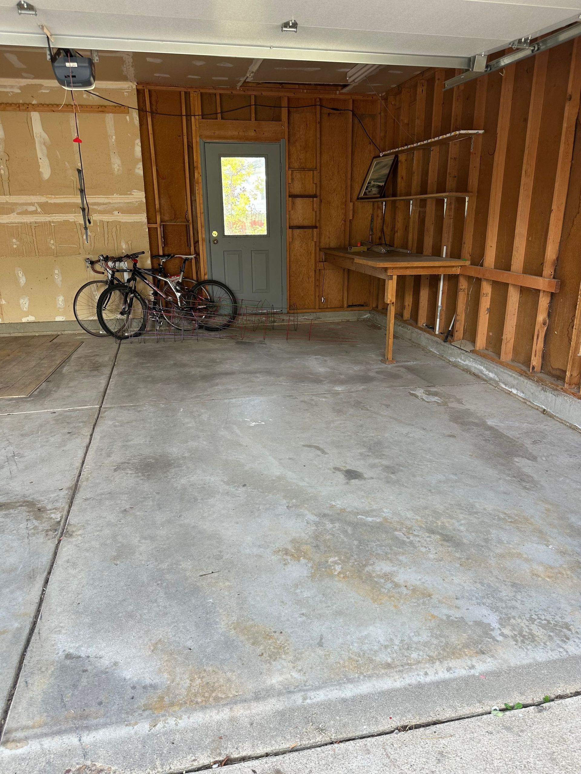 Garage interior with bicycle, door, and workbench. Concrete floor and wood-paneled walls.