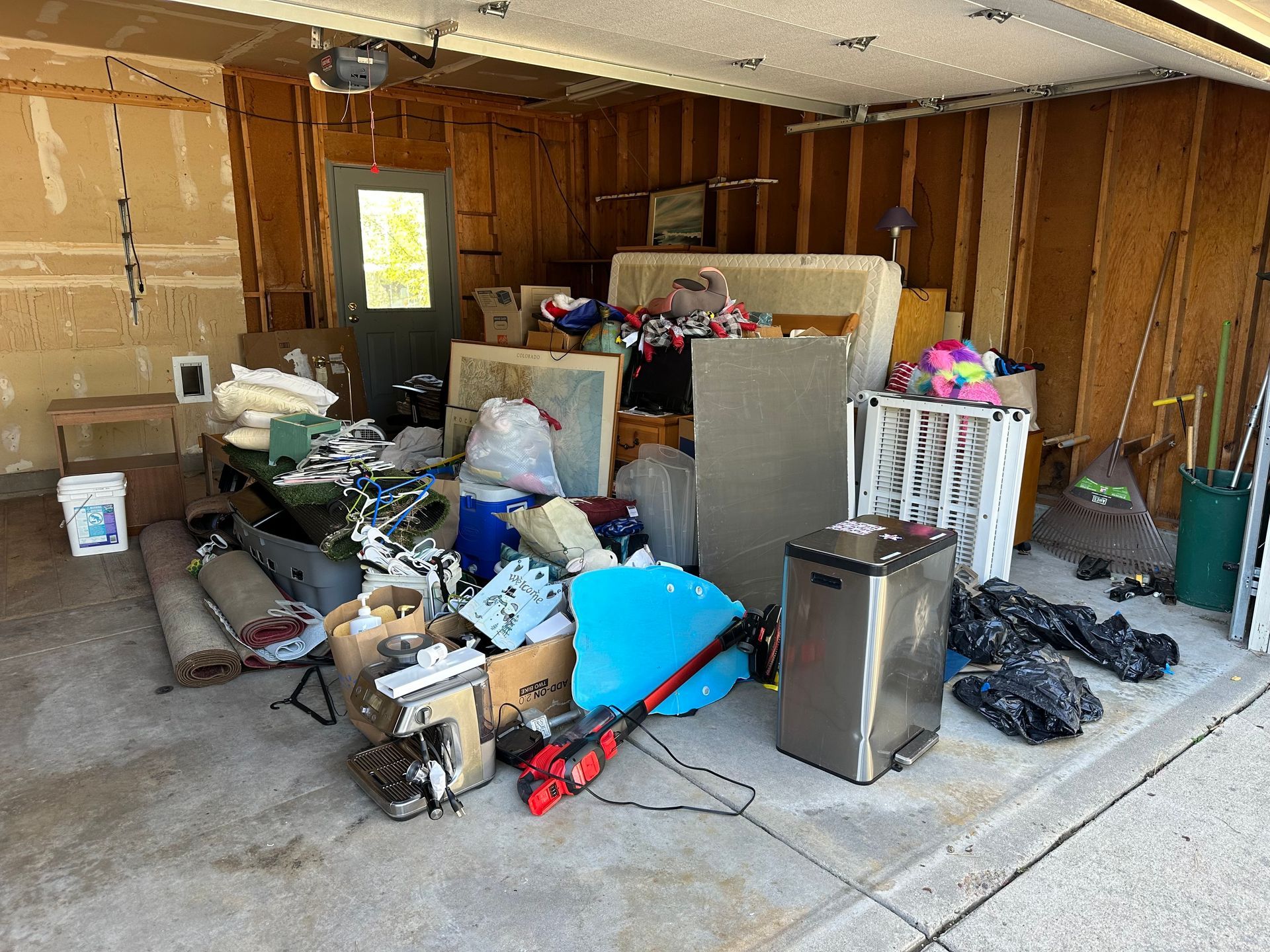 Cluttered garage filled with various items, including boxes, furniture, and tools.