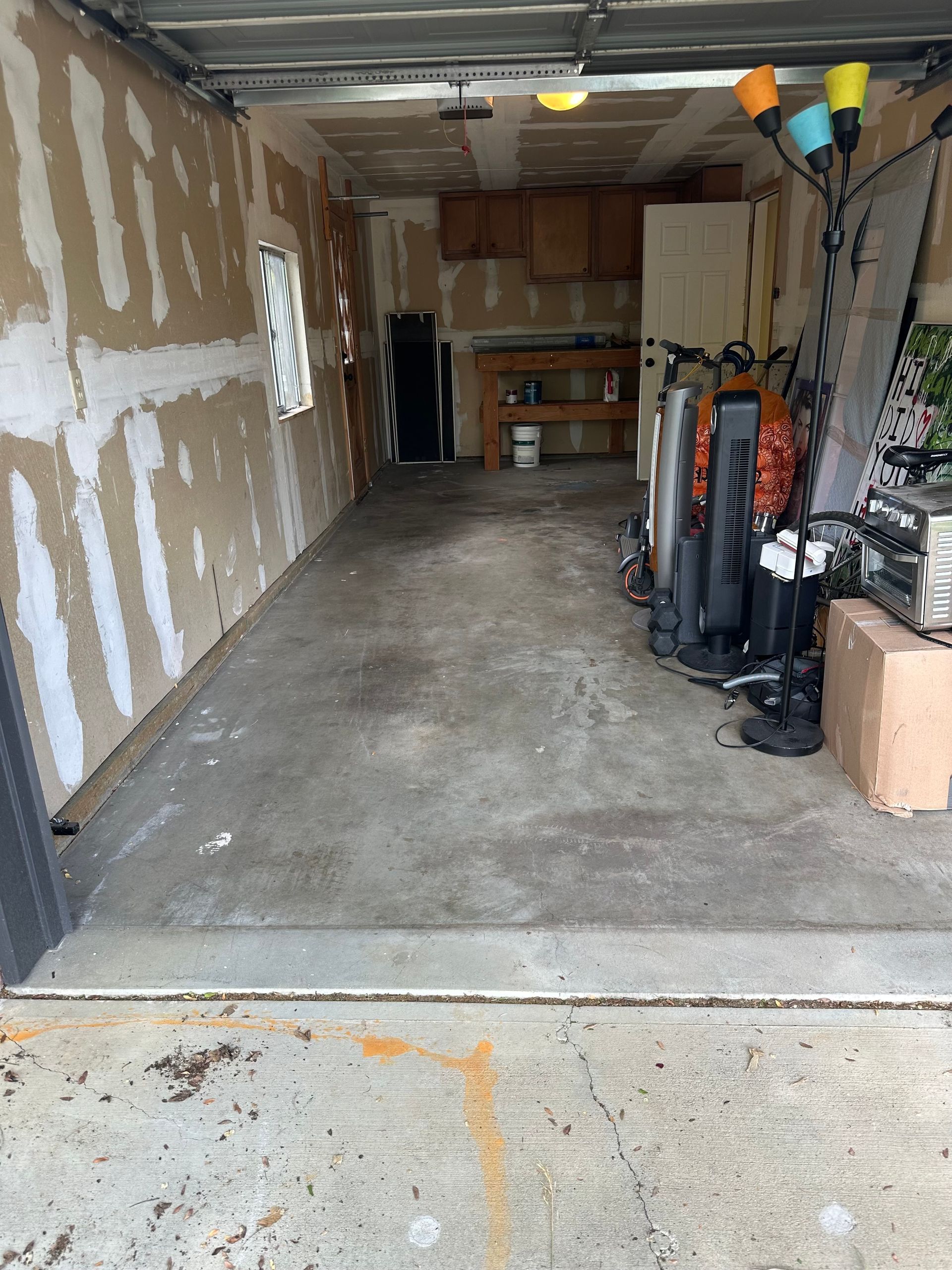 Garage interior with exposed wall studs, concrete floor, and assorted items on the right side.