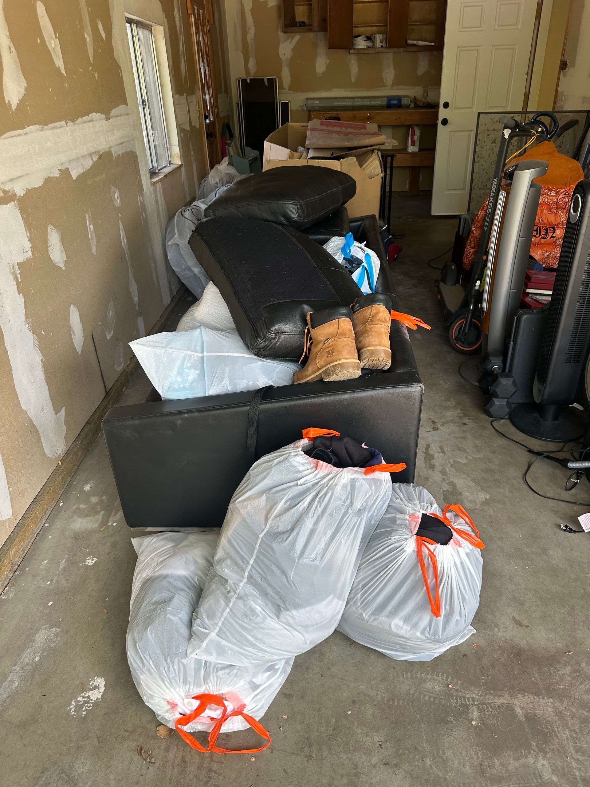 A cluttered garage with a black couch, plastic bags, and various items. A before picture taken in Broomfield, CO.
