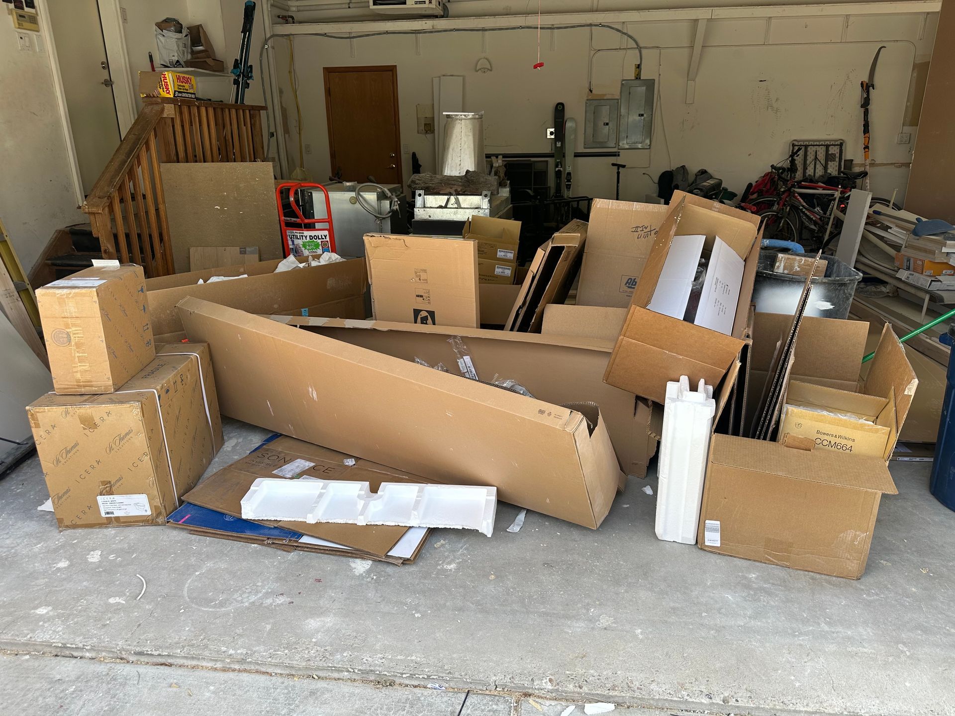 Pile of cardboard boxes on a concrete floor inside a garage. Other items are visible in the background.