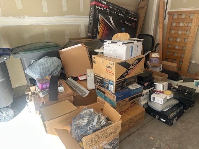 A cluttered garage with boxes, electronics, and a trash bin in Erie, CO.