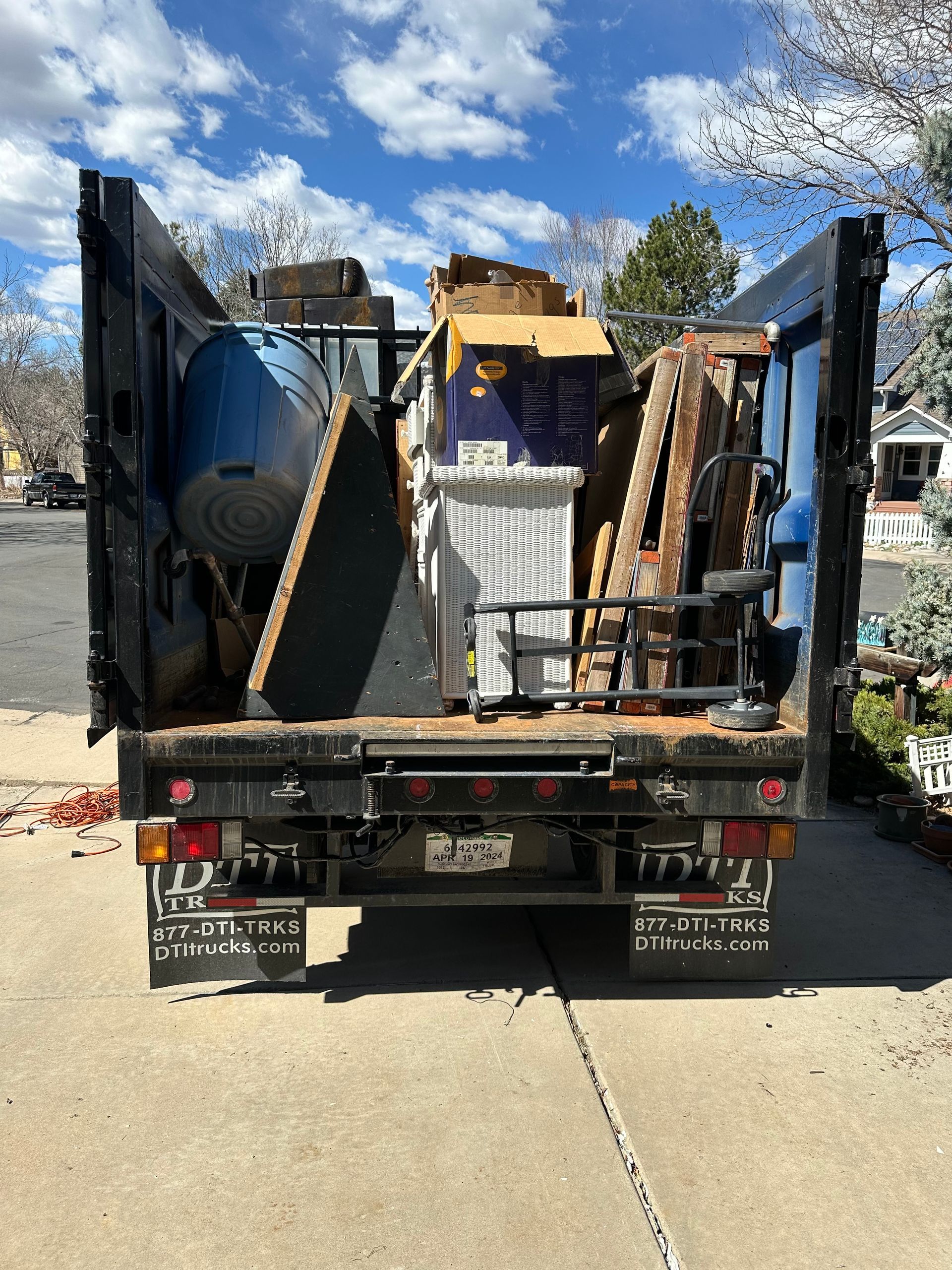 A junk truck filled with lots of junk is parked on the side of the road.