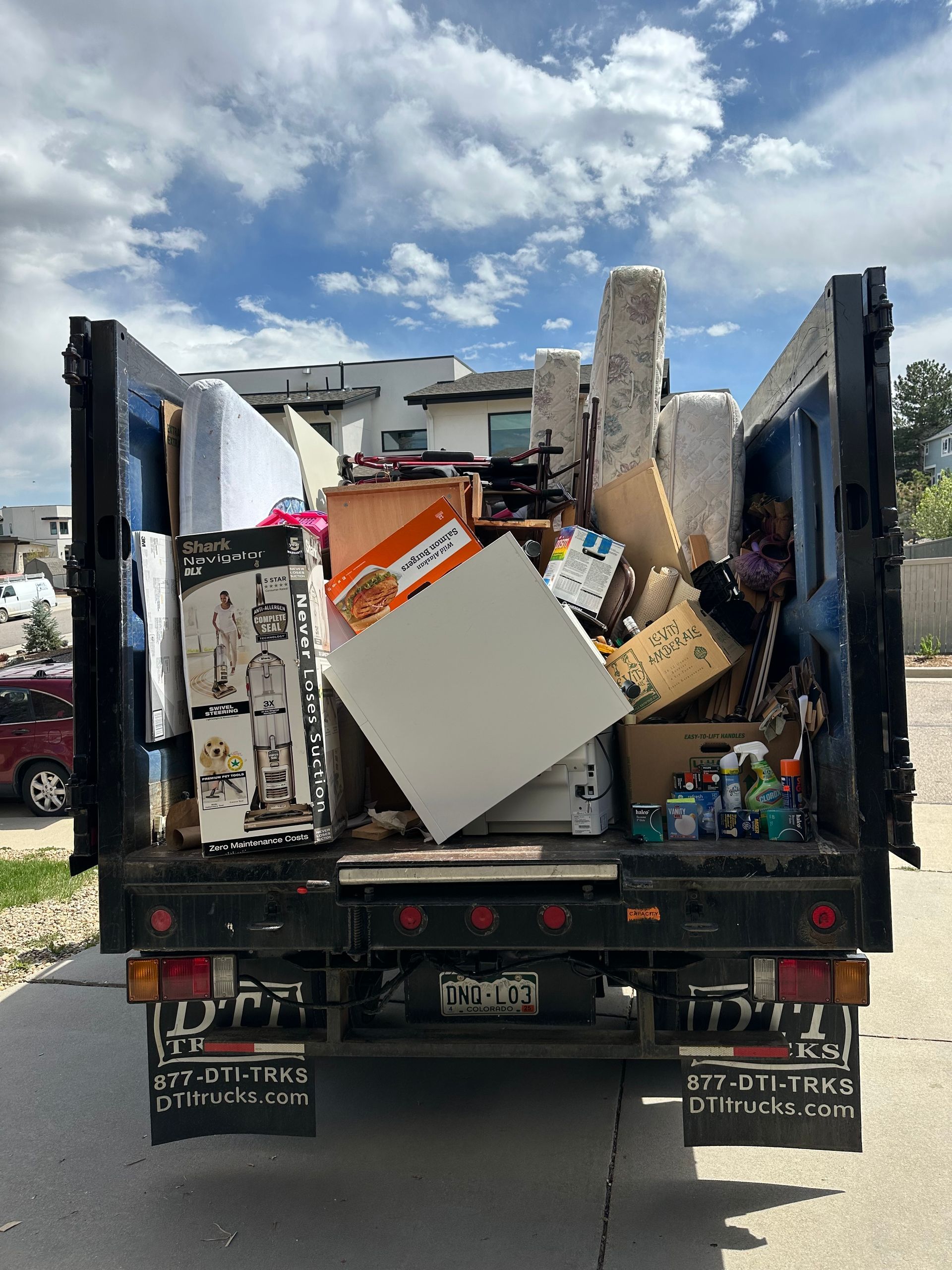 Colorado Junk Runners truck bed overflowing with discarded furniture and household items; blue sky background in Boulder, CO.