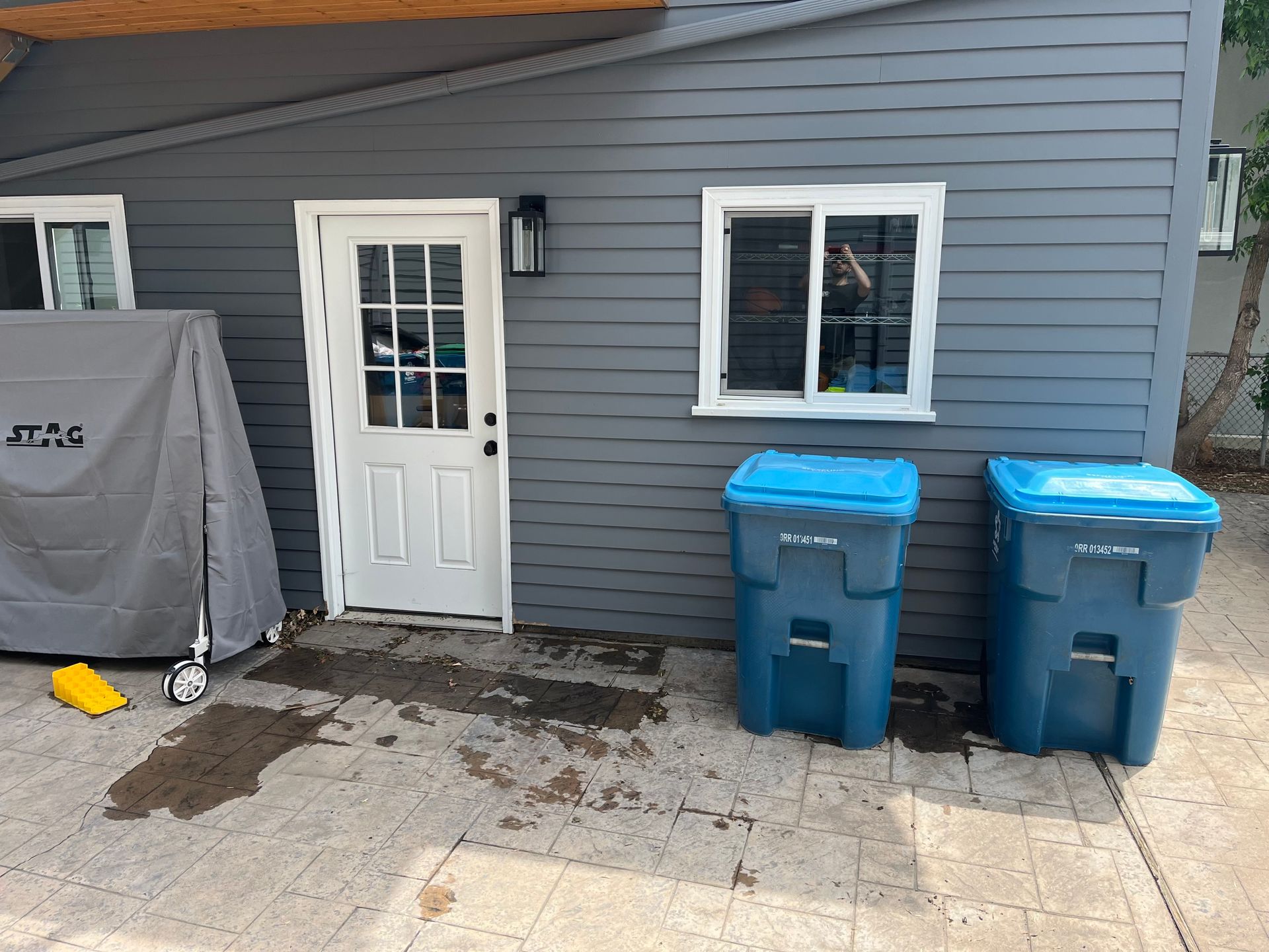 Backyard with blue trash bins, white door, gray siding, and a covered grill. An after picture taken in Arvada, CO.