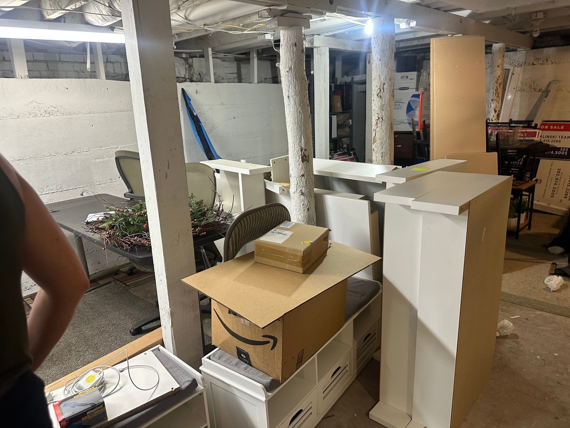 Basement storage room. White pillars, boxes, furniture, and a person looking around the space.