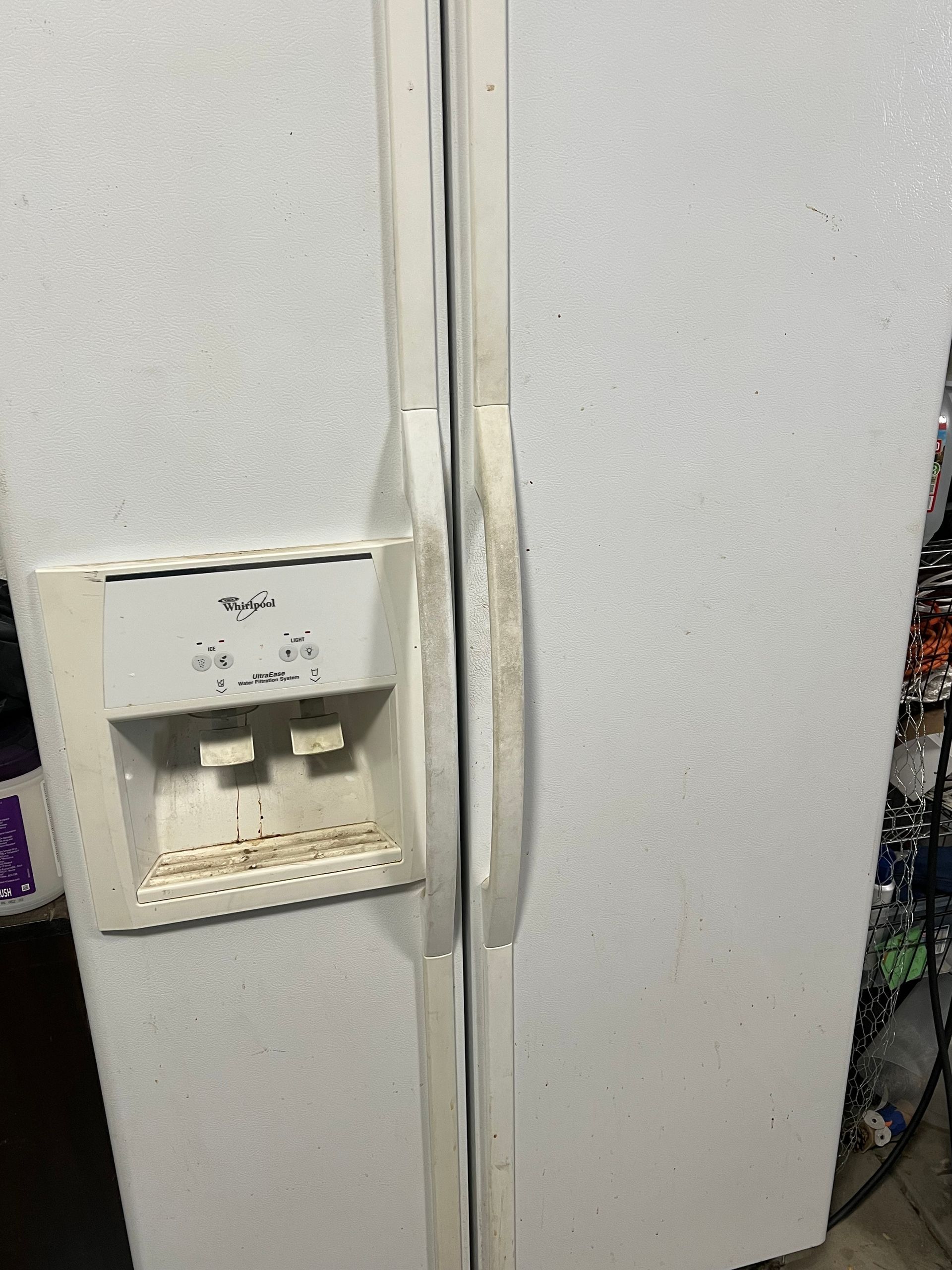 White Whirlpool side-by-side refrigerator with dirty handles and water/ice dispenser in Arvada, CO.
