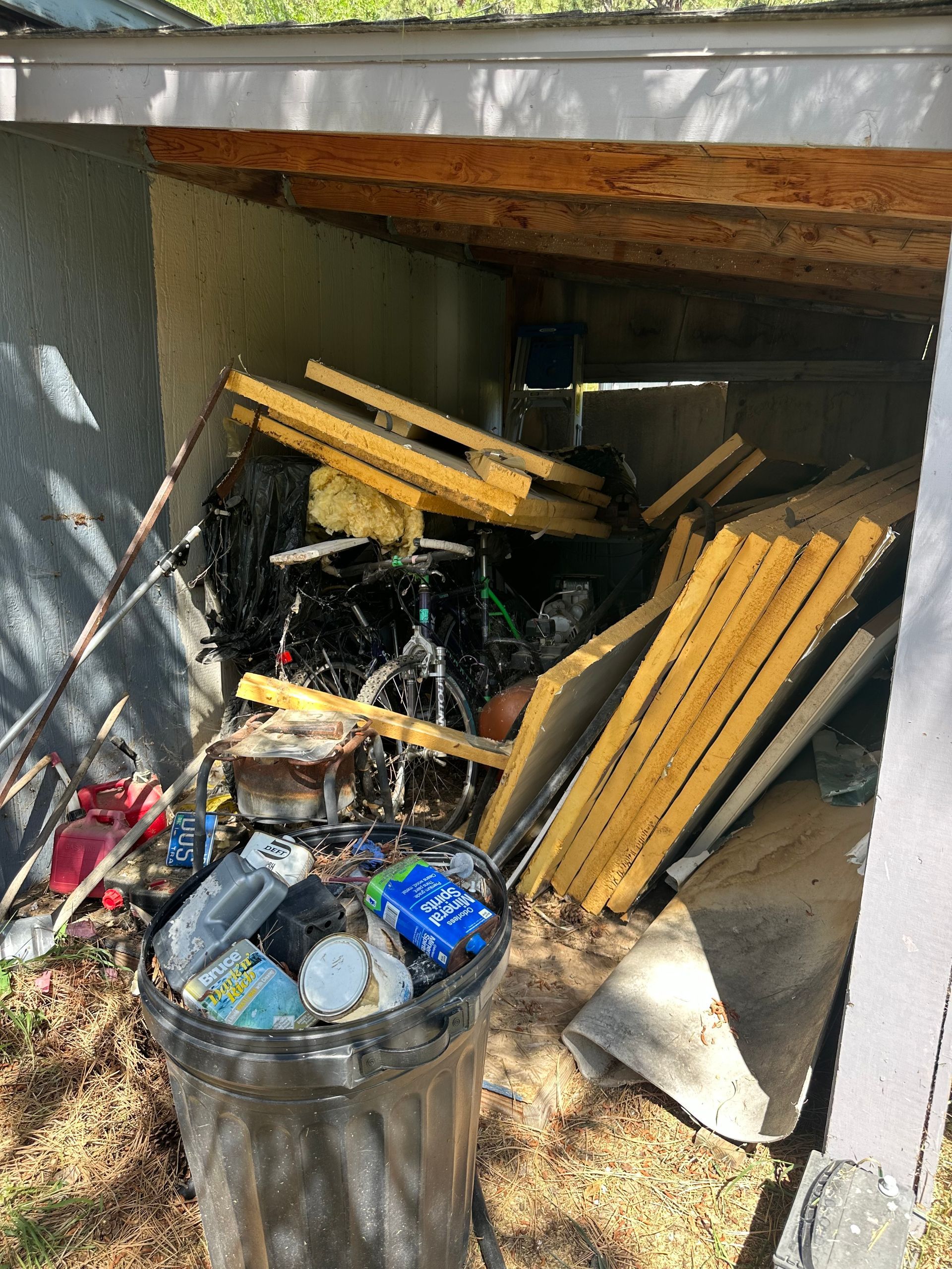 A cluttered storage shed with bikes, trash, and wooden planks in Boulder, CO.